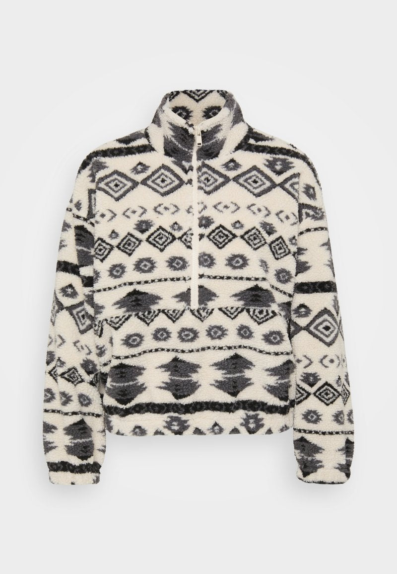 Fleece-Pullover mit hohem Kragen, auf weißem Hintergrund mit schwarzen geometrischen Mustern, einschließlich Rauten und stilisierten Formen.