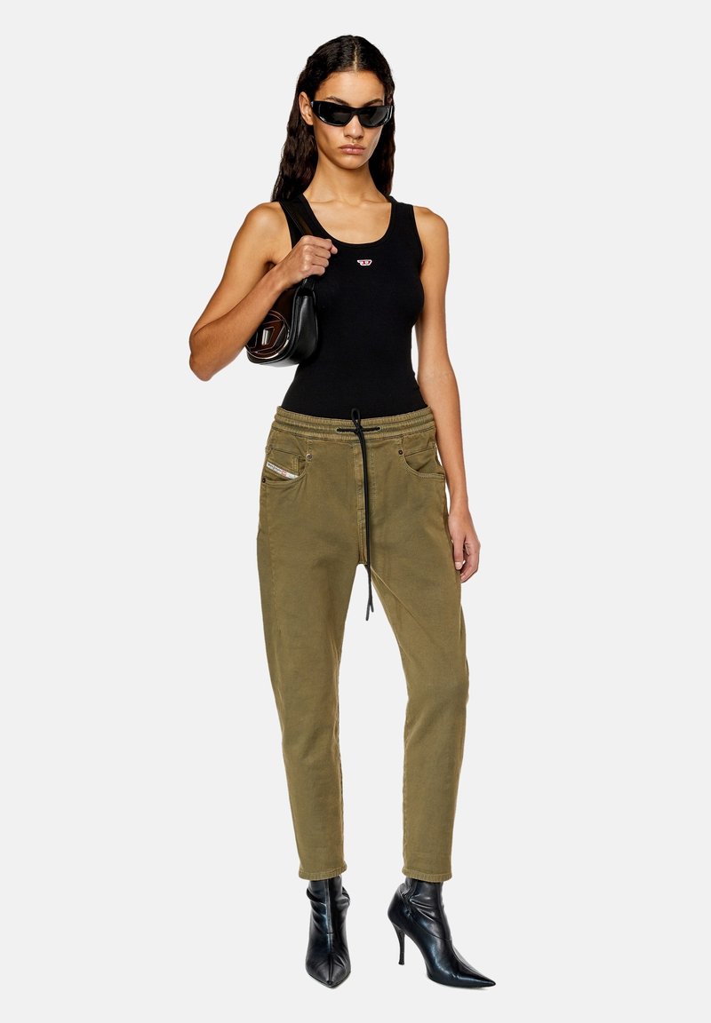 Olivgrüne Jogginghosen mit elastischem Bund, Kordelzug, frontalen Taschen und schmalem Schnitt. Kombiniert mit einem schwarzen Tanktop und Absatzstiefeln.