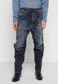 Mann trägt ausgewaschene dunkelblaue Denim-Jogginghosen kombiniert mit schwarzen Schnürschuhen und einem hellblauen, gerippten Langarmshirt.