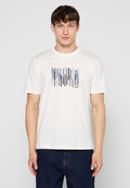 Junger Mann, der ein weißes T-Shirt mit einem mehrfarbigen vertikalen Streifenmuster und dunkelblaue Jeans trägt, steht vor einem schlichten hellen Hintergrund.