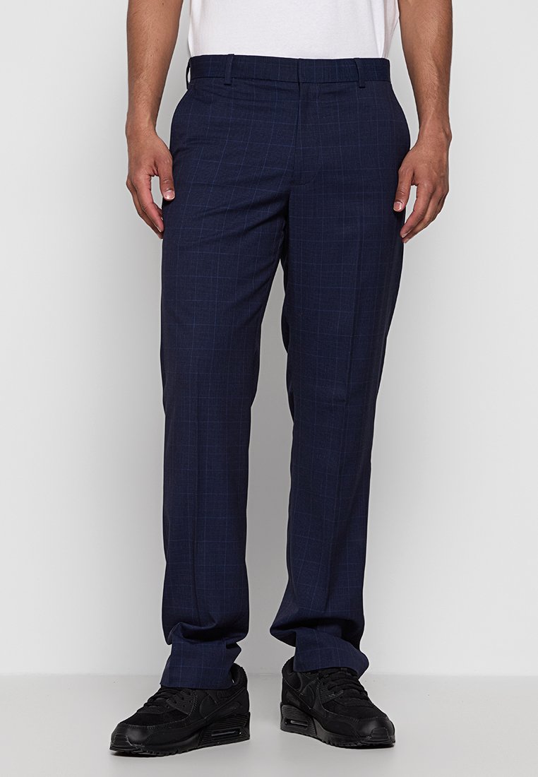 Marineblaue Karohose aus einem strukturierten Stoff, mit geradem Bein und normalem Bund, kombiniert mit schwarzen Sneakers.