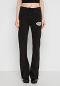 Schwarze Sweatpants mit strukturiertem Rippenmaterial, mit einem Kordelzugbund und einem weißen Patch mit Text am linken Oberschenkel. Eng an den Knöcheln.