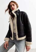 Schwarze Fake-Lederjacke mit cremefarbener Sherpa-Fütterung, Reißverschlusstaschen und einem taillierten Kragen. Strukturiertes Material mit einem verkürzten Design.