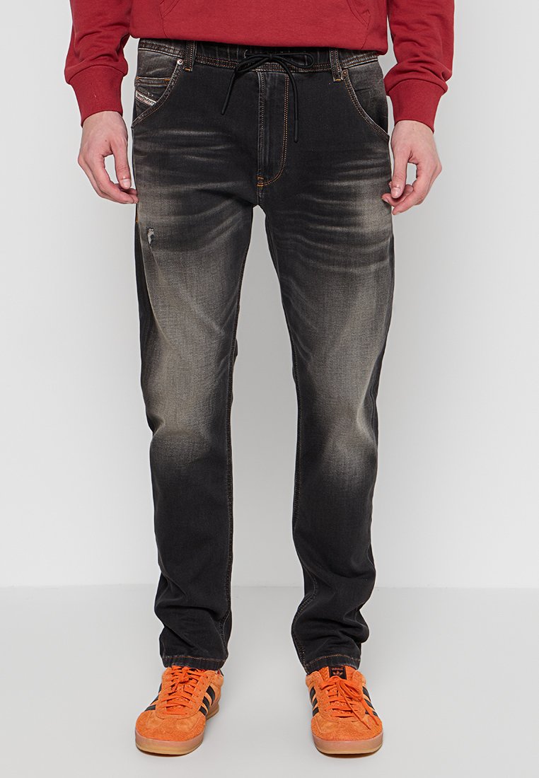 Schwarze Jeans aus Denim mit leichter Ausbleichung, Fünf-Taschen-Design, Kordelzugbund und schmaler Schnitt. Kombiniert mit orangefarbenen Sneakers.