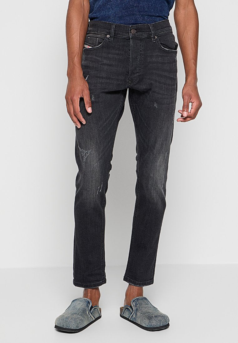 Dunkelgraue Slim-Fit-Jeans mit leichter Ausbleichung und distressed Akzenten, kombiniert mit strukturierten blauen Slippern.