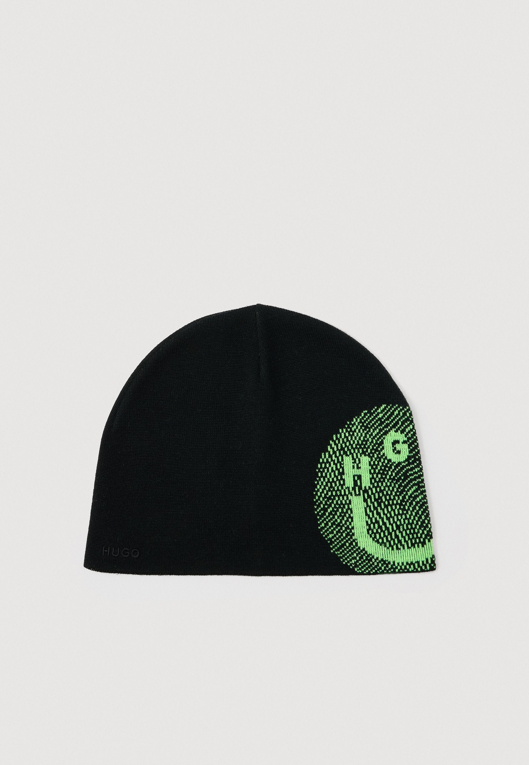 Schwarze Strickmütze mit grünem, pixelartigem Muster, das auf einer Seite die Buchstaben "HUGO" bildet, und kleinem schwarzen "HUGO"-Logo am Rand.