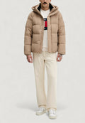 Beige Steppjacke mit Reißverschluss, großen gesteppte Abschnitten und Kapuze. Trägt man über einem weißen Sweatshirt mit Rundhalsausschnitt und beigen Hosen.
