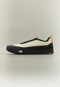 Flacher, zum Hineinschlüpfen geeigneter Outdoorsportschuh in Beige und Schwarz mit orangefarbenen Zuglaschen, dicker Sohle sowie The North Face- und Vibram-Logos.