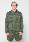 Jacke und Shorts im Tarnmuster in grünen und braunen Tönen. Verfügt über vier Vordertaschen und einen Knopfverschluss. Aus Baumwollmaterial.