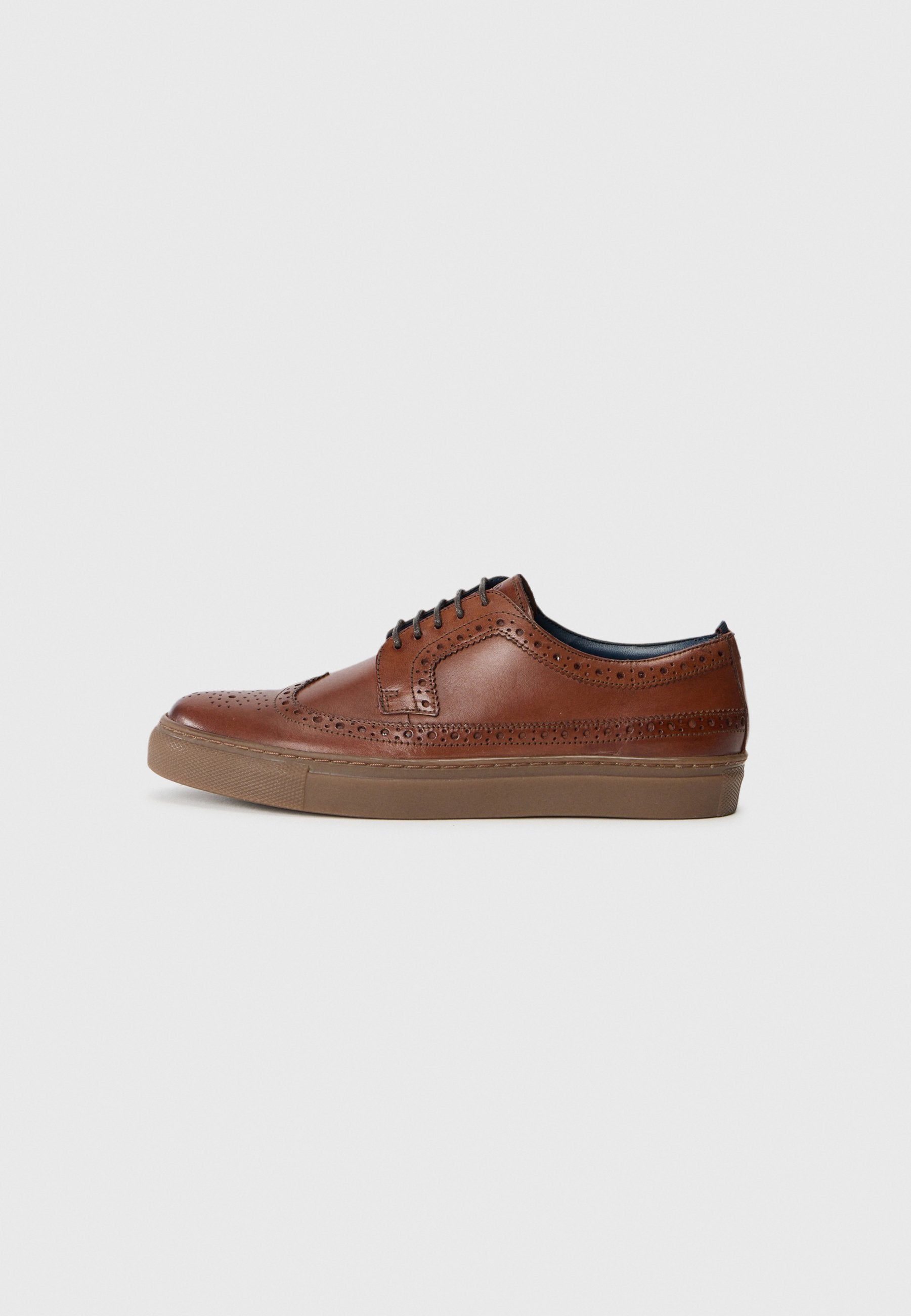 Braune Leder-Brogue-Sneaker mit perforierten Details, schwarzen Schnürsenkeln und einer Gummisohle, seitlich auf einem weißen Hintergrund abgebildet.