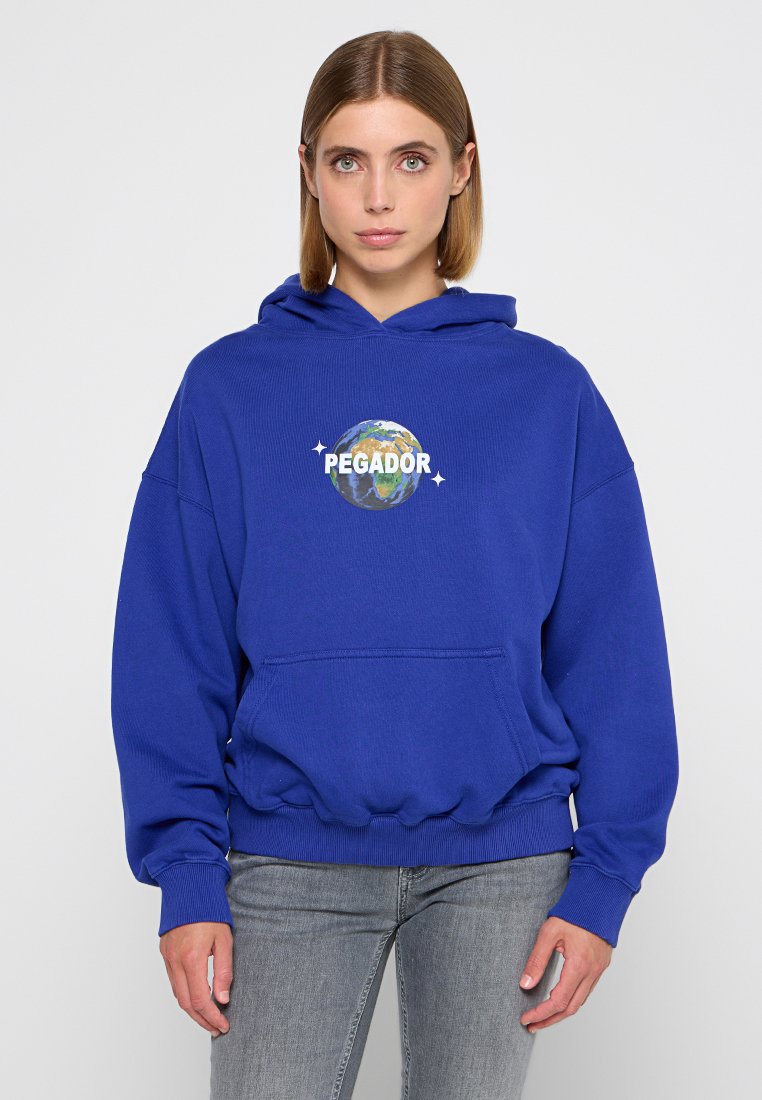Übergroßer blauer Hoodie aus weichem Stoff, mit einer Fronttasche und einem Grafikdesign der Erde mit dem Text "PEGADOR." Rippbündchen und Saum.