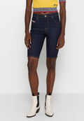 Dunkelblaue Denim-Shorts mit tailliertem Schnitt, ausgestattet mit Gürtelschlaufen, Fronttaschen und gestickten Details. Kombiniert mit einem gelben strukturierten Oberteil und Knöchelstiefeln.