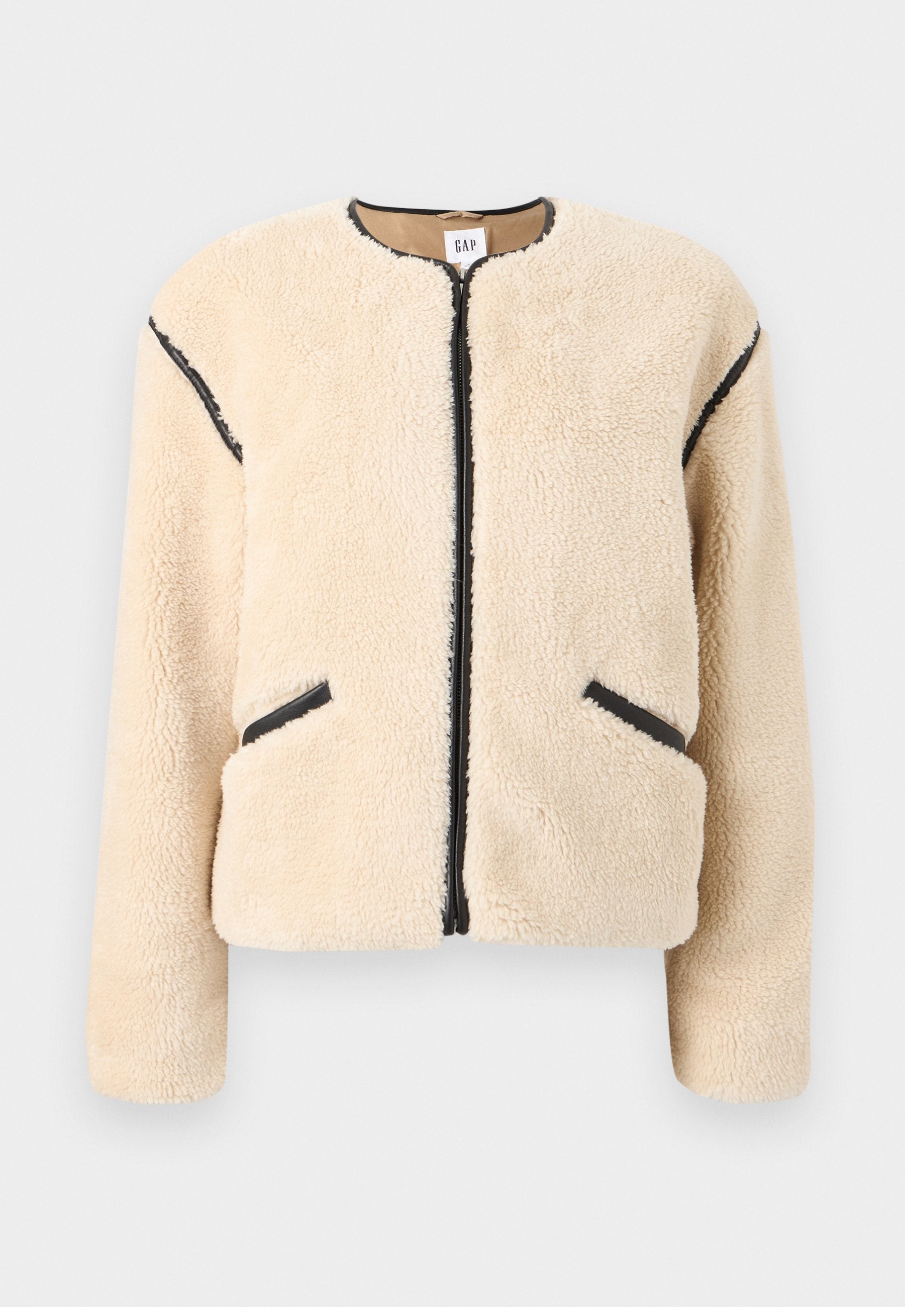 Beige Jacke aus Kunstpelz mit rundem Ausschnitt, Frontreißverschluss, schwarzen Akzenten an den Seiten und zwei Seitentaschen. Weiches, strukturiertes Material.
