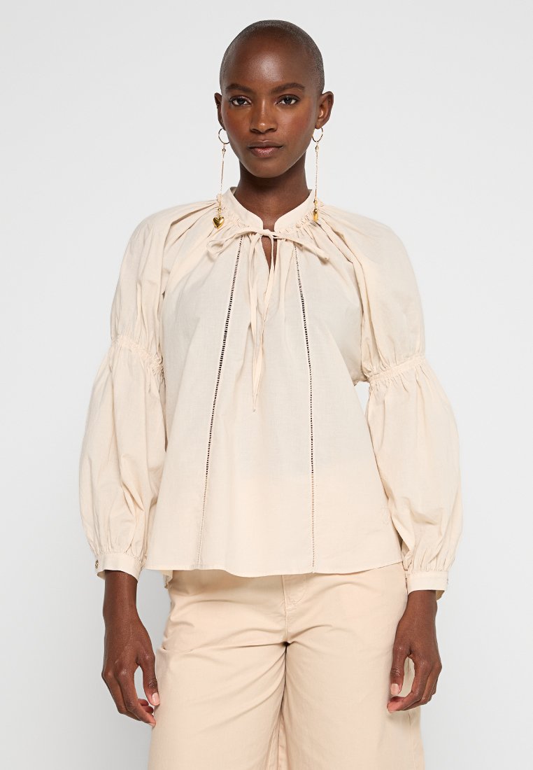 Helles beige Bluse mit Puffärmeln aus weichem Material, mit einem gerafften Ausschnitt, Kordelzug und dezenten Spitzendetails auf der Vorderseite.