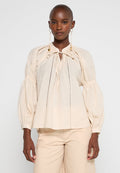 Helles beige Bluse mit Puffärmeln aus weichem Material, mit einem gerafften Ausschnitt, Kordelzug und dezenten Spitzendetails auf der Vorderseite.