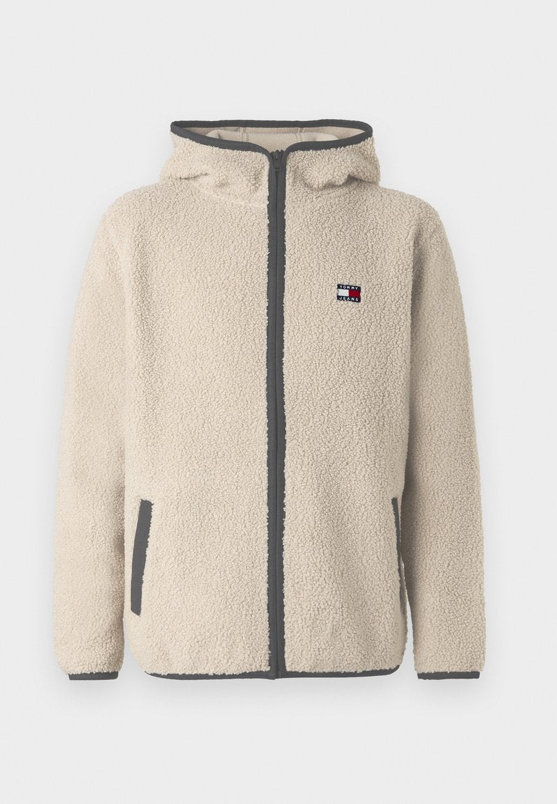 Beige Fleecejacke mit Reißverschluss, Kapuze und grauen Akzenten. Verfügt über seitliche Taschen und ein kleines Logo-Patch auf der Brust. Weiche Textur.