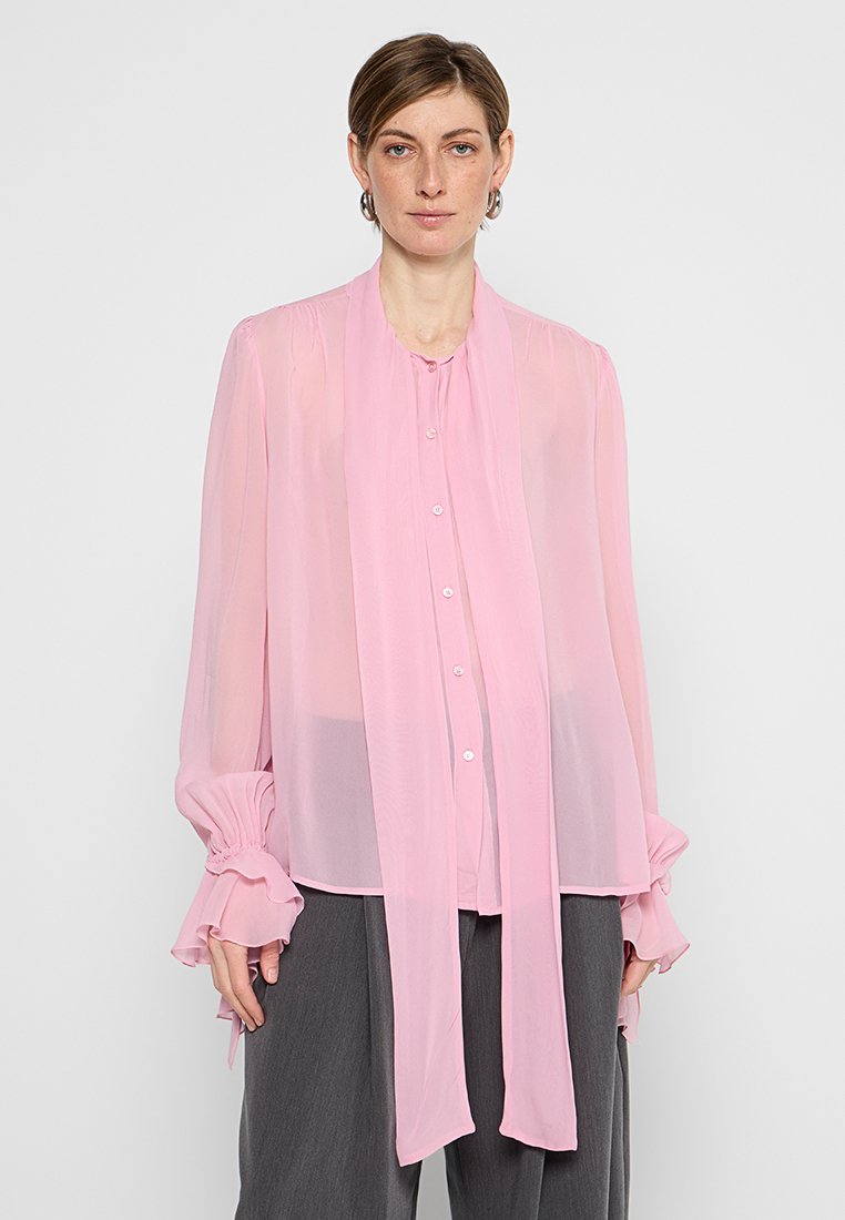 Helles rosa, durchscheinendes Blusenshirt mit langen Ärmeln, Rüschensäumen und Knopfleiste. Verfügt über ein Bindeband am Hals für ein zusätzliches Designelement.