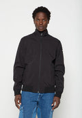 Mann trägt eine schwarze Zip-up-Jacke mit gerippten Bündchen und Saum, steht vor einem schlichten hellen Hintergrund.