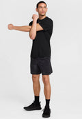 Schwarzes T-Shirt mit kurzen Ärmeln, kombiniert mit schwarzen Shorts mit einem dezenten Muster. Schwarze Sportschuhe und Socken runden das Outfit ab.