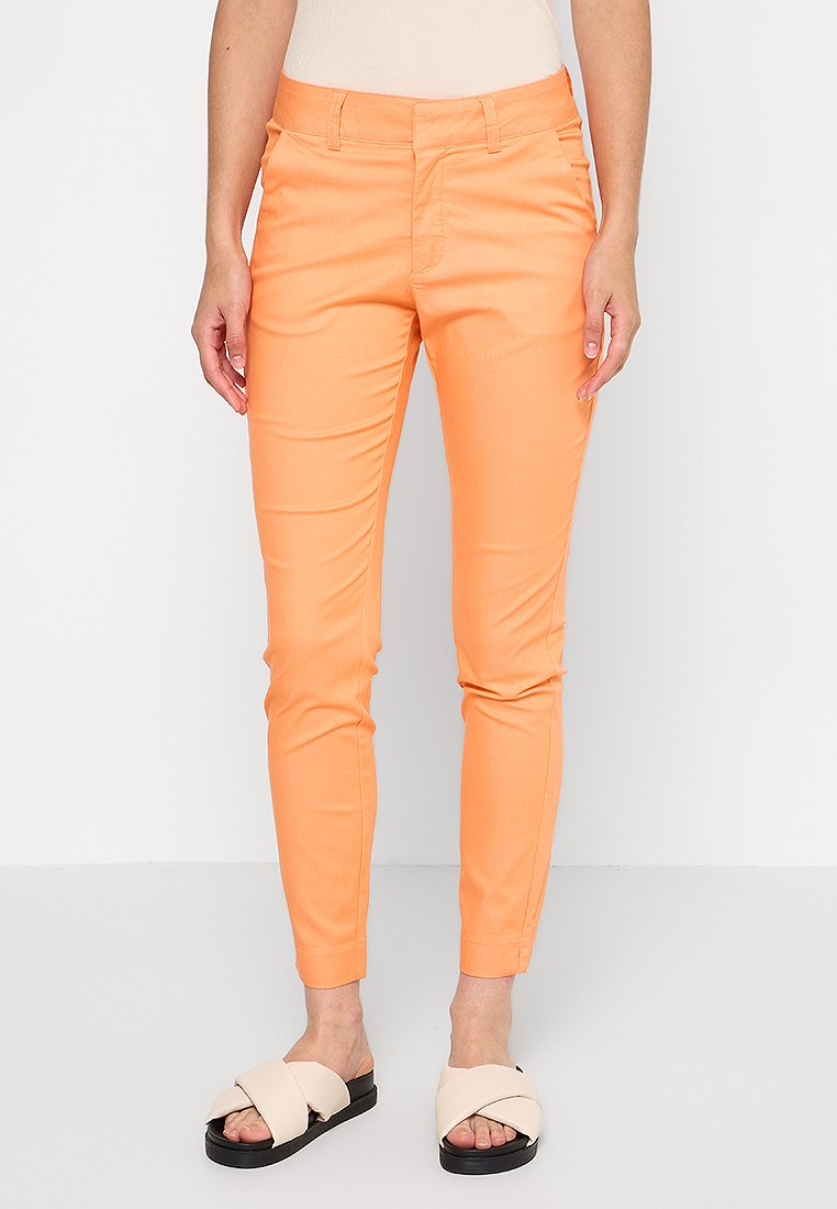 Orange Slim-Fit-Hosen aus dehnbarem Stoff, ausgestattet mit Gürtelschlaufen, Seitentaschen und einer glatten Textur. Kombiniert mit cremefarbenen Sandalen.