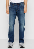 Dunkelblaue Jeans aus Denim mit geradem Schnitt, dezentem Fade-Effekt, fünf Taschen und einem Knopfverschluss. Getragen mit grauen Sneakers.