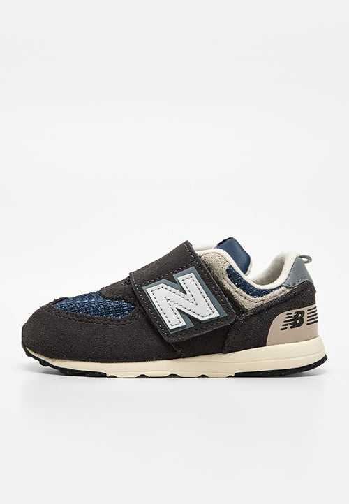 Kinderschuh von New Balance in Schwarz und Marineblau mit Klettverschluss, beiger Sohle und gepolstertem Innenfutter vor weißem Hintergrund.