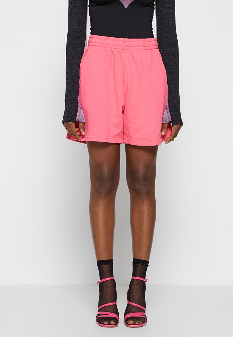 Rosa Baumwollshorts mit einem elastischen Bund und Seitentaschen; kombiniert mit einem Langarmoberteil aus strukturiertem schwarzem Stoff mit lila Akzenten.