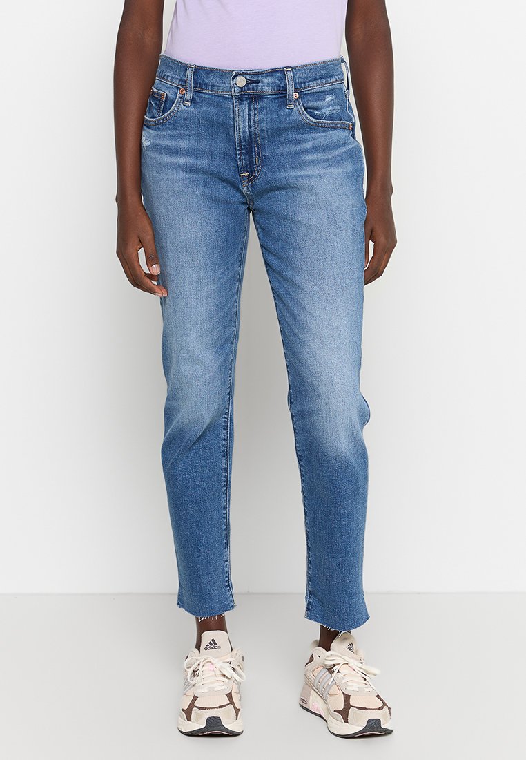 Helle blaue Jeans im Straight-Leg-Stil mit hoher Taille und leichten Used-Effekten an den Oberschenkeln, kombiniert mit sneakers in neutralen Farbtönen.