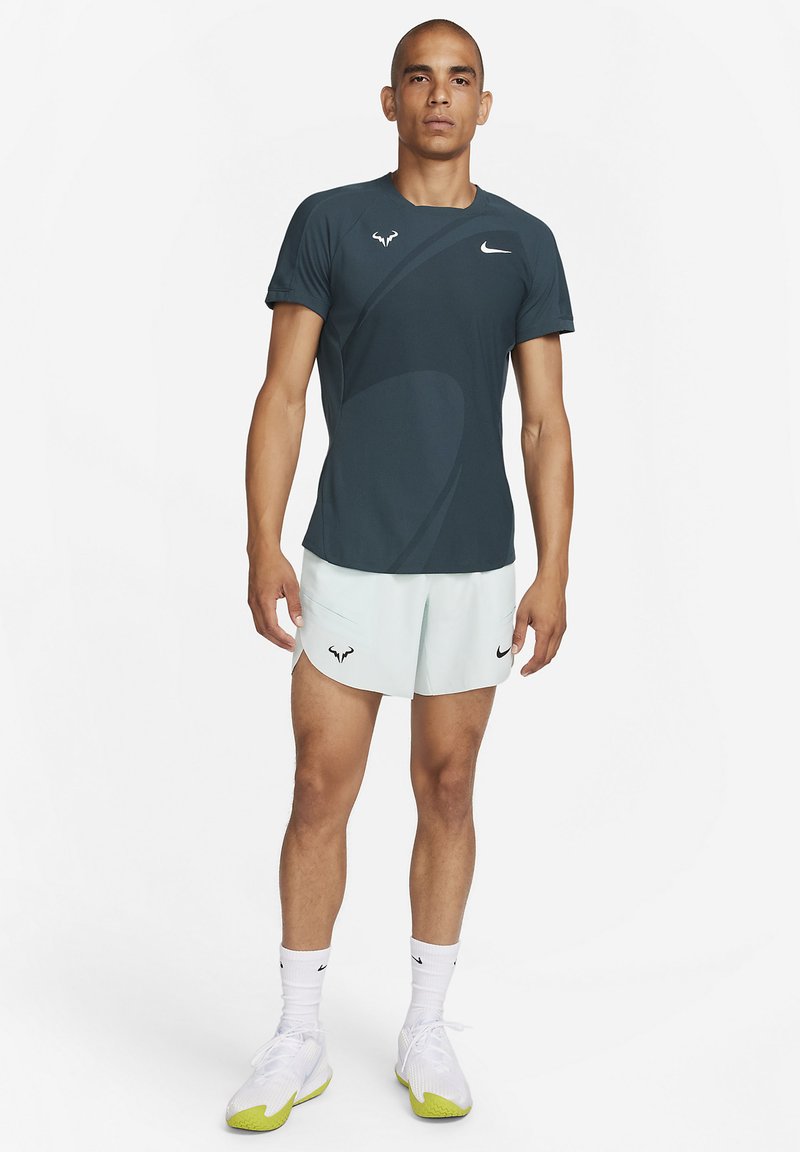 Männliches Sportoutfit mit einem dunkelgrünen Kurzarmshirt mit Nike-Logo und hellmintfarbenen Shorts, beide aus leichtem Material.