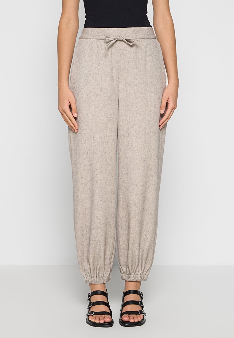 Hellbeige, taillierte Jogginghosen mit elastischen Bündchen, einem Kordelzugbund und einem strukturierten Stoff. Getragen mit schwarzen Riemchensandalen.
