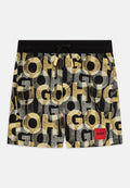 Schwarze Badeshorts mit einem grafischen Muster aus großen, sich überlappenden Buchstaben in Gelb und Grau. Enthält ein rotes Logopatch und einen Kordelzug in der Taille.