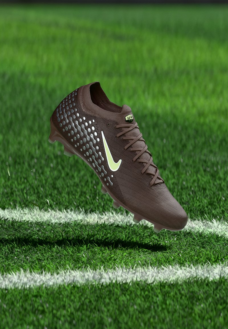 Brauner Fußballschuh mit weißem Logo und strukturierten Seiten, schwebend über einem grünen Rasenfeld nahe der weißen Grenzlinie.