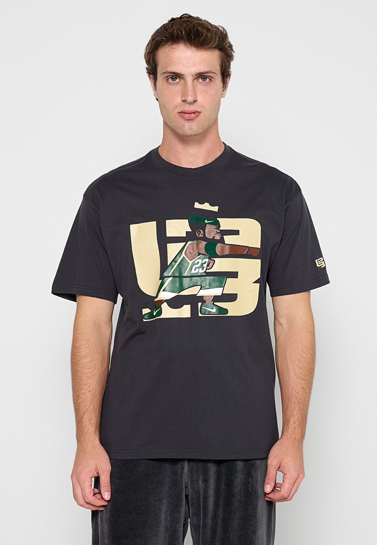 Junger Mann trägt ein schwarzes T-Shirt mit einer Grafik eines Basketballspielers in grüner Uniform und der Nummer 23 vorne.