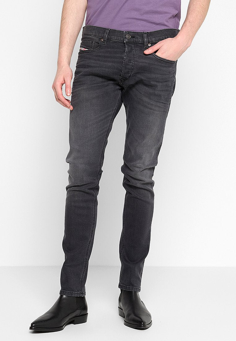 Dunkelgraue Denim-Jeans im Slim-Fit, mit Reißverschluss, fünf Taschen und dezenten Ausbleichungen. Getragen mit schwarzen Knöchelstiefeln.