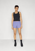 Schwarzes, kurzes Tanktop mit seitlichen Ausschnitten, kombiniert mit helllilafarbenen Sportshorts mit elastischem Bund und weißem Logo. Schwarze Turnschuhe.