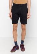 Schwarze Baumwollshorts mit geradem Schnitt, zwei Seitentaschen und umgeschlagenem Saum. Kombiniert mit burgunderfarbenen Sneakers und blauen Akzenten.