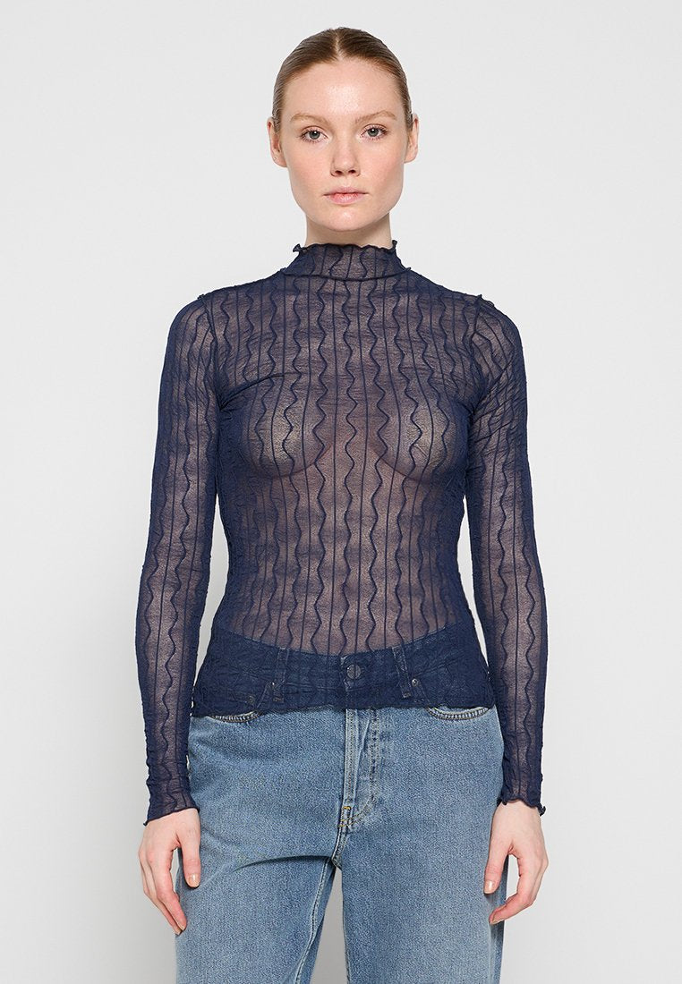 Marineblaue Langarmbluse aus einem strukturierten, transparenten Stoff mit wellenförmigen Mustern, einem hohen Kragen und einer taillierten Passform. Kombiniert mit Jeans.