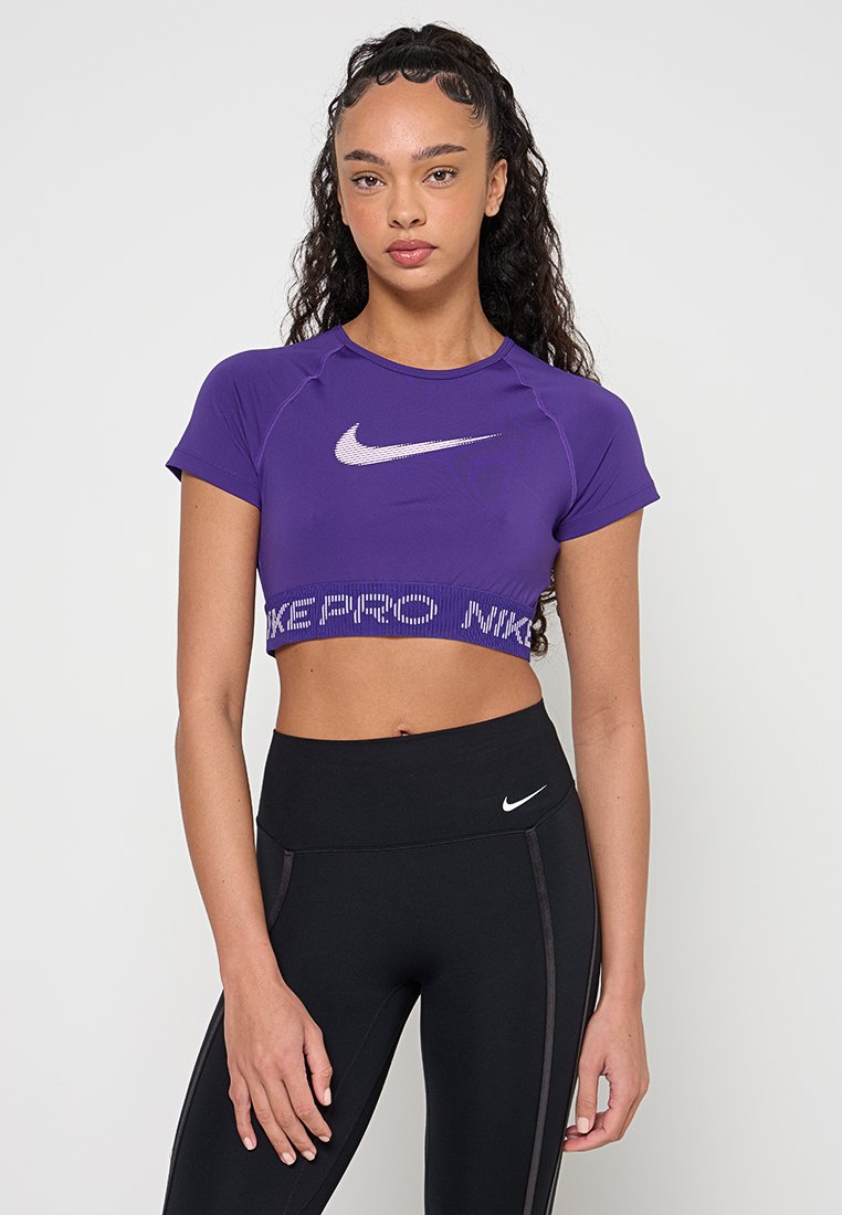 Lila Nike Crop-Top mit kurzen Ärmeln, weißem Logo und strukturierter Taillenpartie. Kombiniert mit hoch taillierten schwarzen Leggings mit Logodetail.