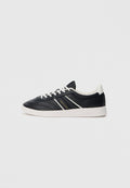 Schwarze Ledersneaker mit weißen Akzenten, die ein niedriges Design, eine runde Zehenpartie und eine strukturierte Oberfläche aufweisen. Mit goldenem Logo an der Seite.