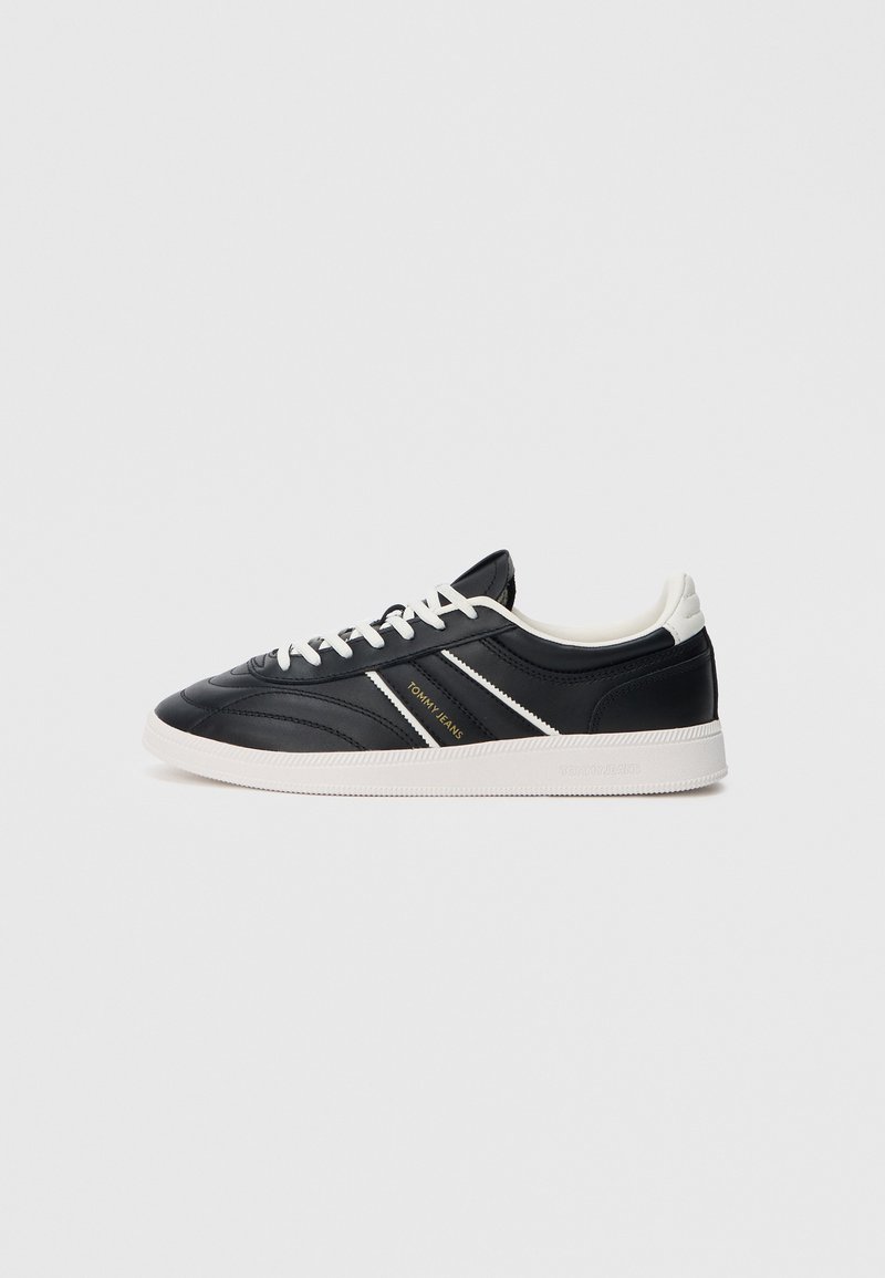 Schwarze Ledersneaker mit weißen Akzenten, die ein niedriges Design, eine runde Zehenpartie und eine strukturierte Oberfläche aufweisen. Mit goldenem Logo an der Seite.