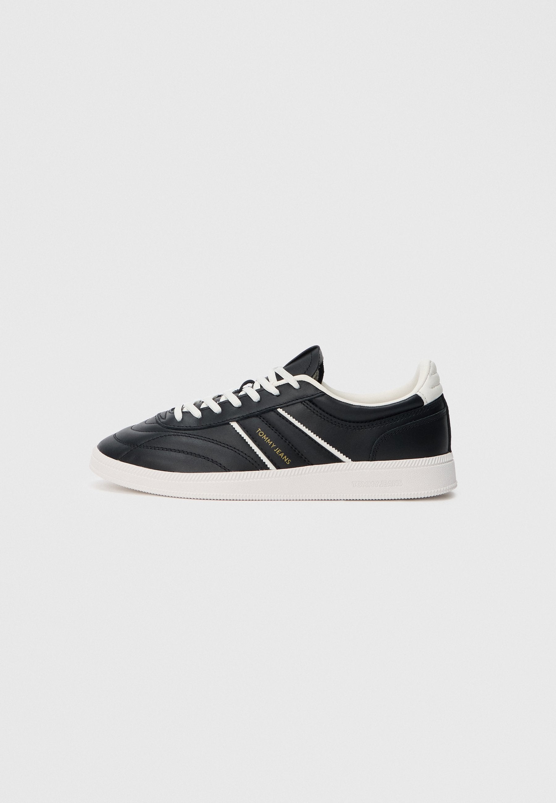 Schwarze Ledersneaker mit weißen Akzenten, die ein niedriges Design, eine runde Zehenpartie und eine strukturierte Oberfläche aufweisen. Mit goldenem Logo an der Seite.