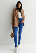 Beige oversized Blazer, weißes, enges Oberteil, blaue Skinny-Jeans, weiße Sneakers und eine kleine braune Handtasche. Glatte Texturen und maßgeschneidertes Design.