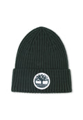 Dunkelgrüne gerippte Mütze mit umgeschlagenem Rand. An der Vorderseite befindet sich ein runder weißer Aufnäher mit einem Baum-Logo. Weiche Stricktextur.