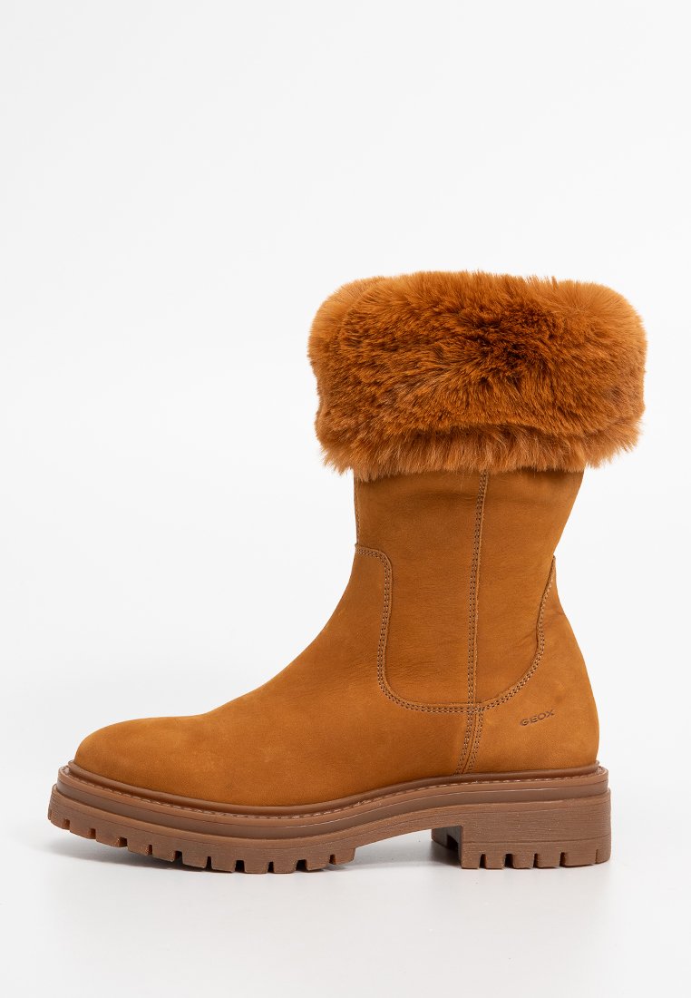 Beige Wildleder-Ankle-Boot mit einem weichen, braunen Fellkragen, strukturierter Gummisohle und seitlichen elastischen Einsätzen für einen bequemen Einstieg. Markenlogo an der Seite.