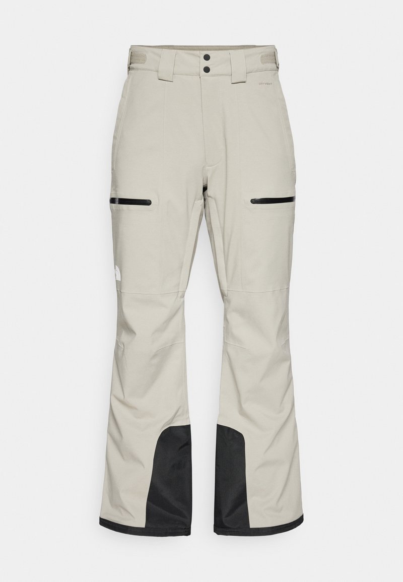 Helle beige Schneehosen mit schwarzen Akzenten, ausgestattet mit einem verstellbaren Taillenbund, zwei seitlichen Taschen mit Reißverschlüssen und verstärkten schwarzen Unterbeinen.