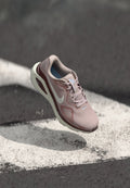 Hellrosa und kastanienbrauner Nike-Laufschuh schwebt über Asphalt mit weißen Markierungen und zeigt Sohle- und Seitendetails.