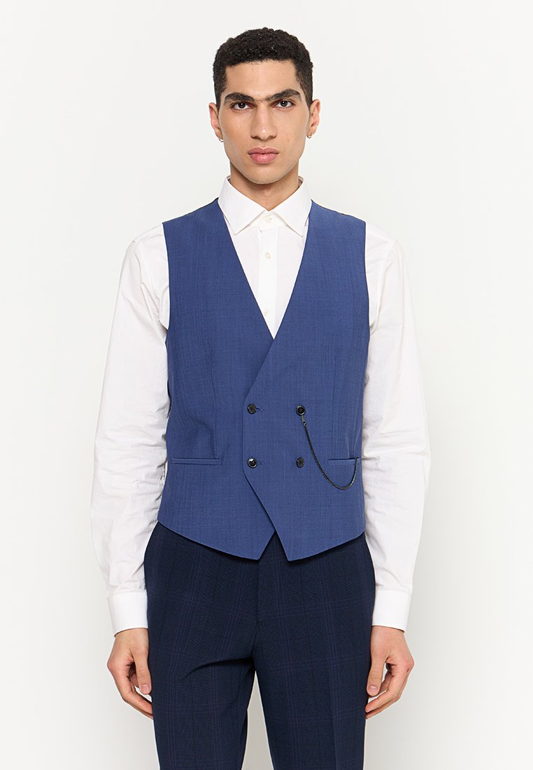 Blaues, doppelt knöpfbares Weste mit strukturiertem Finish, ausgestattet mit einer Kettendetail und schwarzen Knöpfen, getragen über einem weißen Hemd und navy Hosen.