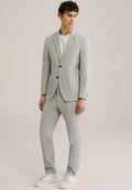 Hellgrauer Anzug mit strukturiertem Finish, einreihiger Blazer und passender Hose. Trägt darunter ein weißes T-Shirt und kombiniert mit weißen Sneakers.