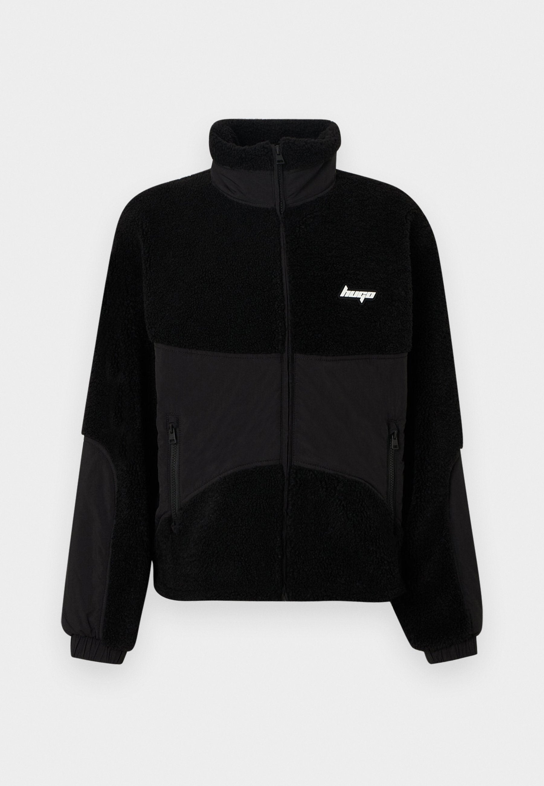 Schwarze Fleecejacke mit hohem Kragen, kontrastierenden schwarzen Stoffpanelen, seitlichen Reißverschlusstaschen und kleinem Logo auf der Brust.