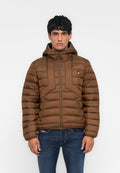 Mann trägt eine braune, gesteppte Jacke mit Kapuze, Frontreißverschluss und seitlichen Reißverschlusstaschen, kombiniert mit blauen Jeans, steht vor einem einfarbigen Hintergrund.